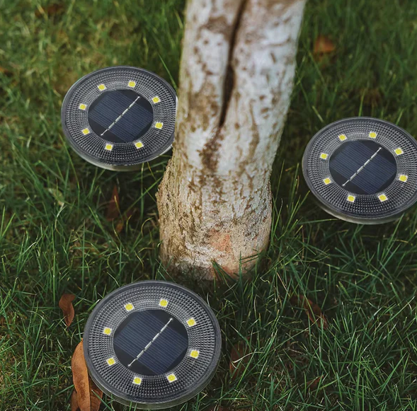 Three solar-powered outdoor lights on grass next to a tree stump