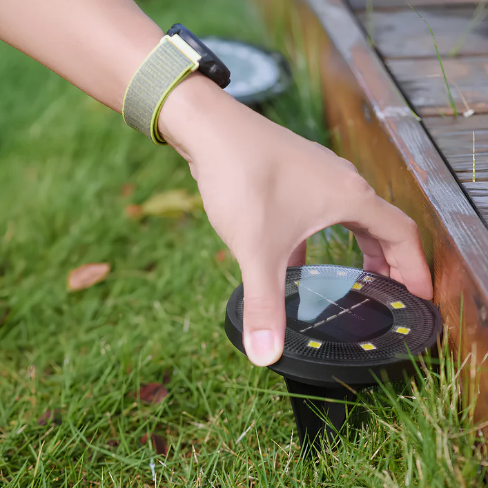 Hand placing a solar-powered outdoor light on grass