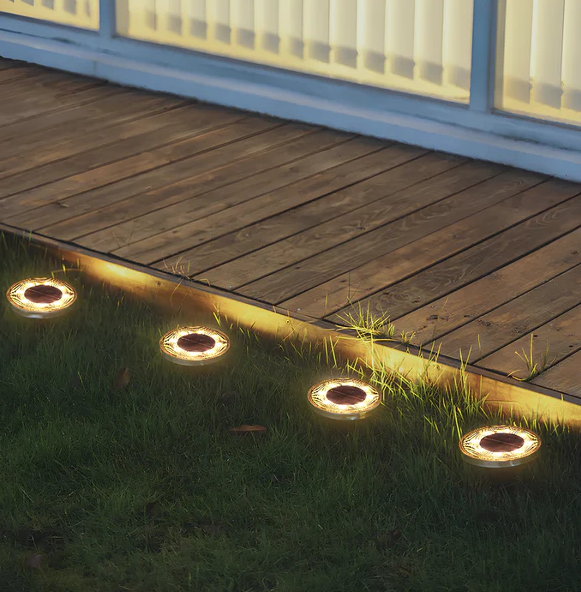 Solar-powered outdoor lights embedded in a wooden deck with grass.